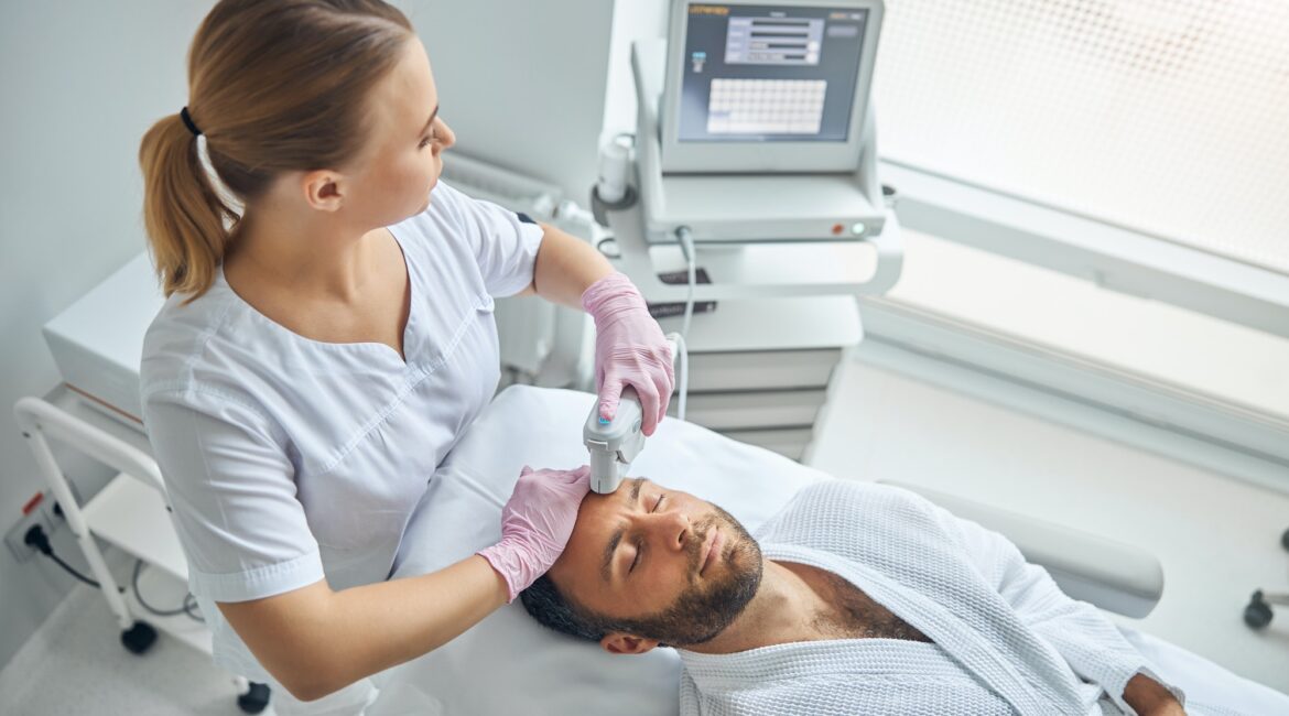 Handsome young man receiving laser facial treatment in cosmetological clinic